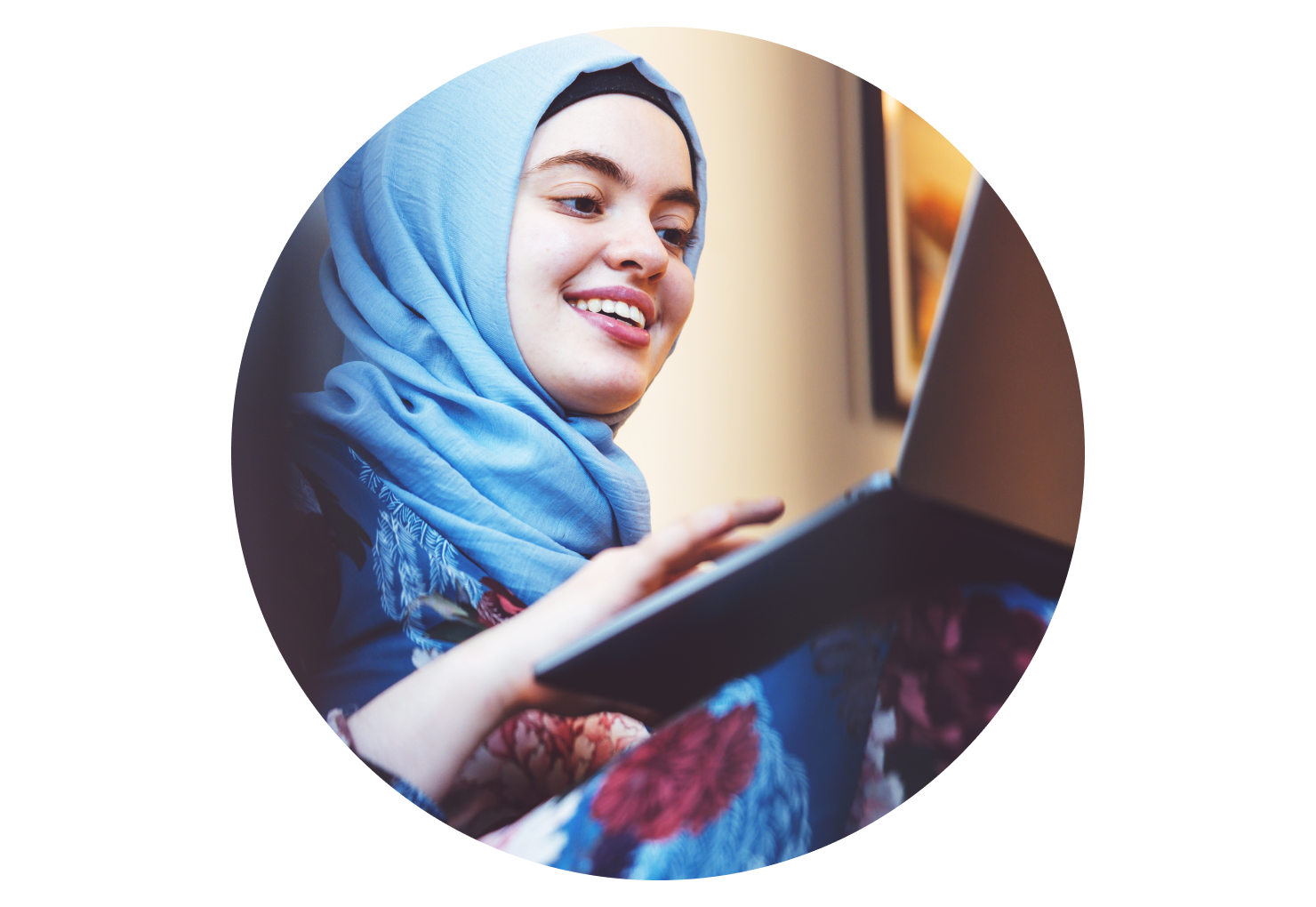 A smiling student works on a laptop balanced on their lap