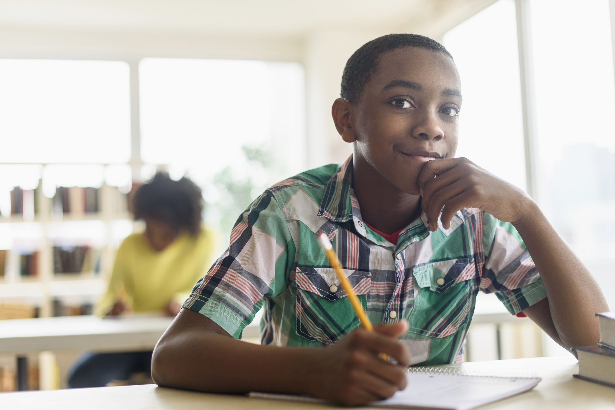 A young student holding a pencil over his notebook and smiling into the camera.